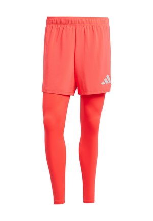 Rote Sportshorts mit elastischem Bund, die über passenden roten Leggings getragen werden. Verfügt über ein kleines silbernes Logo an der Seite der Shorts.