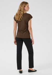 Brun topp med korta ärmar tillsammans med svarta byxor med raka ben. Tyget verkar mjukt, med en enkel design utan synliga mönster eller utsmyckningar.