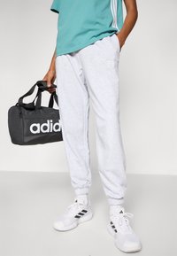 Hallid trenningpüksid pehmest kangast, elastsete mansettidega, koos türkiissinise T-särgiga ja musta Adidas duffeli kotiga.