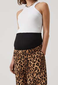 Vit ribbad linne med en svart elastisk midja, kombinerad med bruna byxor i leopardmönster med elastisk midja och sidfickor.