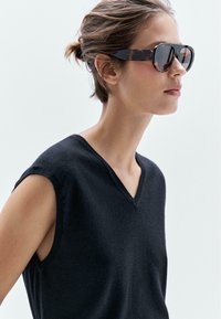 Black sleeveless V-neck top made of soft fabric, paired with tortoiseshell sunglasses. Model's hair is styled in a casual updo.
