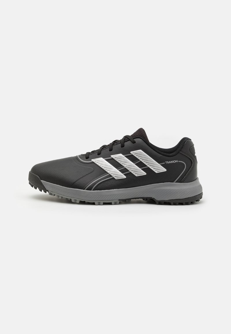 Zapatilla deportiva negra con parte superior texturizada, franjas plateadas, cierre de cordones y suela de goma gris con picos de tracción.