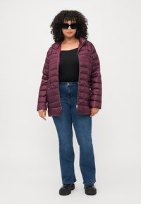 Maroon puffer jacket with a zippered front, featuring a smooth texture and quilted pattern. Paired with dark blue flared jeans and black shoes.