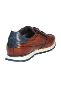 Chaussure en cuir marron avec un design perforé, accents navy au talon, semelle intermédiaire blanche et semelle extérieure bleu foncé. Présente des lacets et un détail de fermeture éclair.