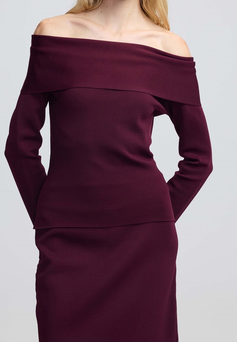 Top bordeaux con spalle scoperte e maniche lunghe, caratterizzato da una texture liscia e un design a strati. Silhouette aderente che si estende fino alla vita.