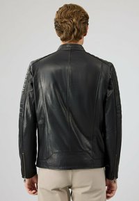 Zwarte leren jas met een slank ontwerp, voorzien van gequiltte accenten op de schouders, ritssluitingen bij de mouwen en een soepele textuur. Achteraanzicht weergegeven.