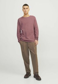 Bordeaux gebreide longsleeve shirt gecombineerd met bruine geplooide broek en donkere sneakers. De outfit heeft een ontspannen pasvorm en een zachte textuur.