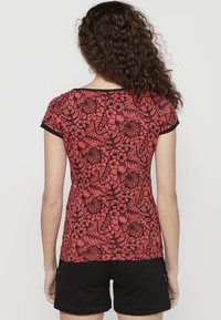 Haut à motifs floraux rouges avec des accents noirs et des manches courtes, fabriqué en tissu léger avec une silhouette moulante.