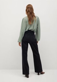 Jasnozielona bluzka z bufkami i marszczonym tyłem, w połączeniu z czarnymi dżinsami o wysokim stanie i szerokimi nogawkami oraz brązowymi botkami na obcasie.