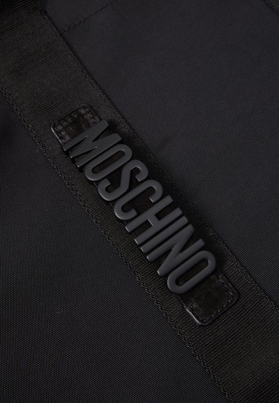 Must mustkott musta kangast, mille rihmal on tekstuuriga, väljaulatuv "MOSCHINO" logo. Pind on sile ja nähtav õmblus.