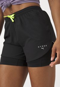 Pantaloni scurți atletici negri cu o croială slim, având un tiv elastic, șnur de culoare verde neon și logo-ul alb "HYROX" pe laterale.