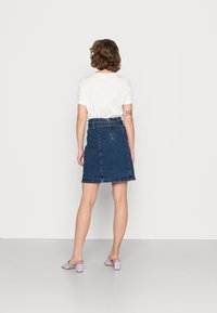 Saia de ganga azul escura com cintura alta, detalhe de fecho éclair na frente e bainha desfiada, combinada com uma t-shirt branca simples e sandálias de salto de cor lilás claro.