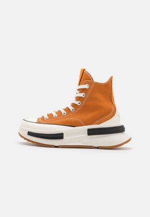Oranger High-Top-Canvas-Sneaker mit dicker weißer Sohle, schwarzen Akzenten, weißen Schnürsenkeln und sichtbaren weißen Nähten auf einfachem Hintergrund.