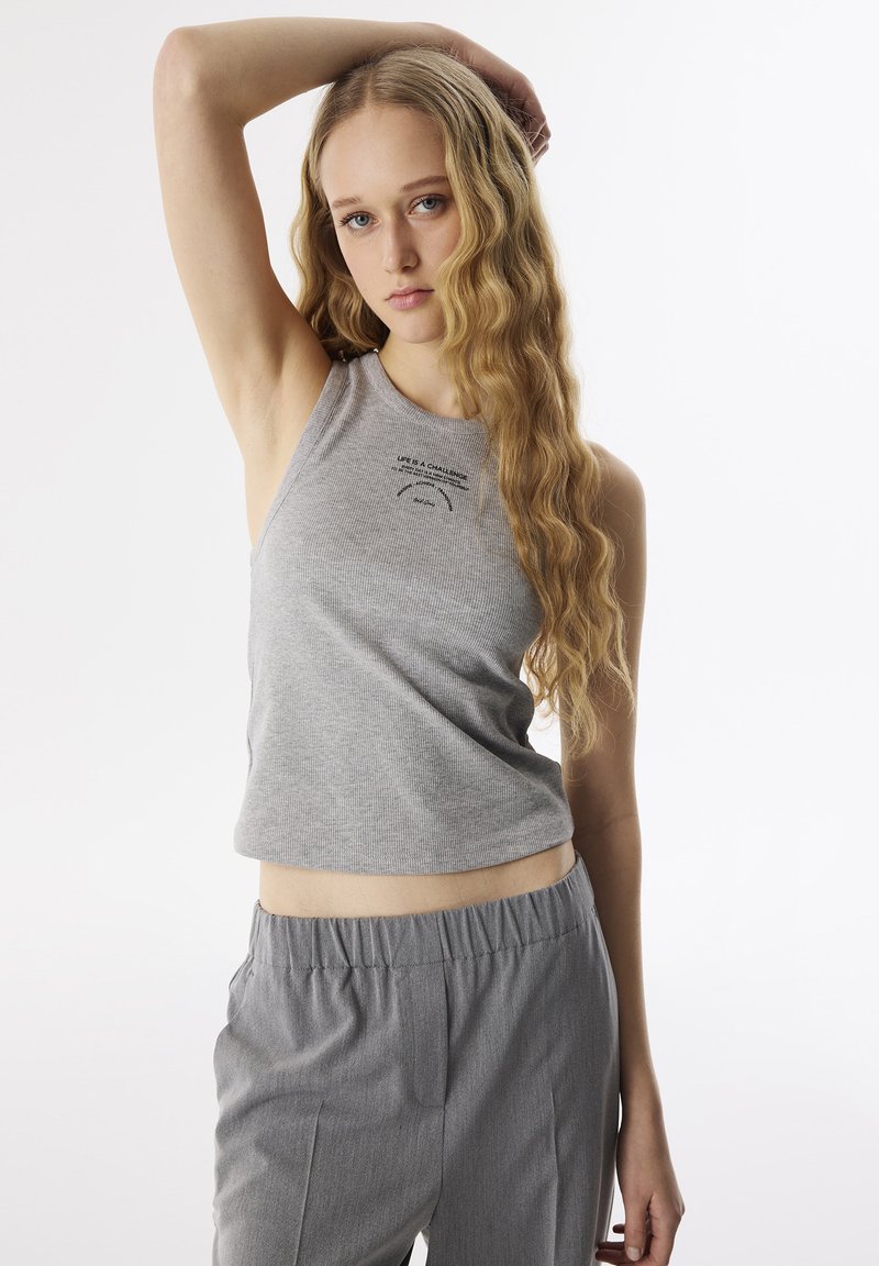 Top in cotone grigio a coste con scollatura rotonda e orlo corto, con un motivo stampato nella zona del petto. Abbinato a pantaloni grigi con vita elastica.