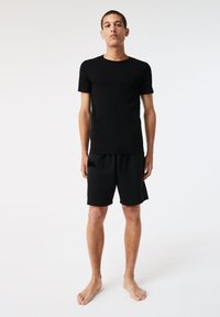 T-shirt nera a girocollo abbinata a pantaloni sportivi neri con un piccolo logo. Tessuto leggero, design aderente e maniche corte.