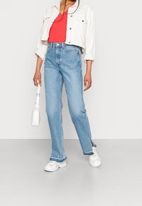 Kort vit denimjacka, röd linne, ljusblå högmidjade jeans med sidofickor, vita sneakers och en liten vit handväska.