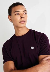 T-shirt en coton violet avec une coupe classique, présentant un logo "Lee" brodé en blanc sur la poitrine et des manches courtes.