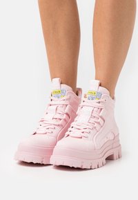Różowe buty wysokie z grubą gumową podeszwą, teksturowaną cholewką, metką z logo oraz szczegółowym systemem sznurowania. Odpowiednie do codziennego noszenia.