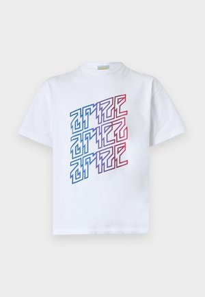 Hombre con camiseta blanca con texto geométrico colorido y pantalones deportivos negros descoloridos, de pie frente a un fondo blanco liso.
