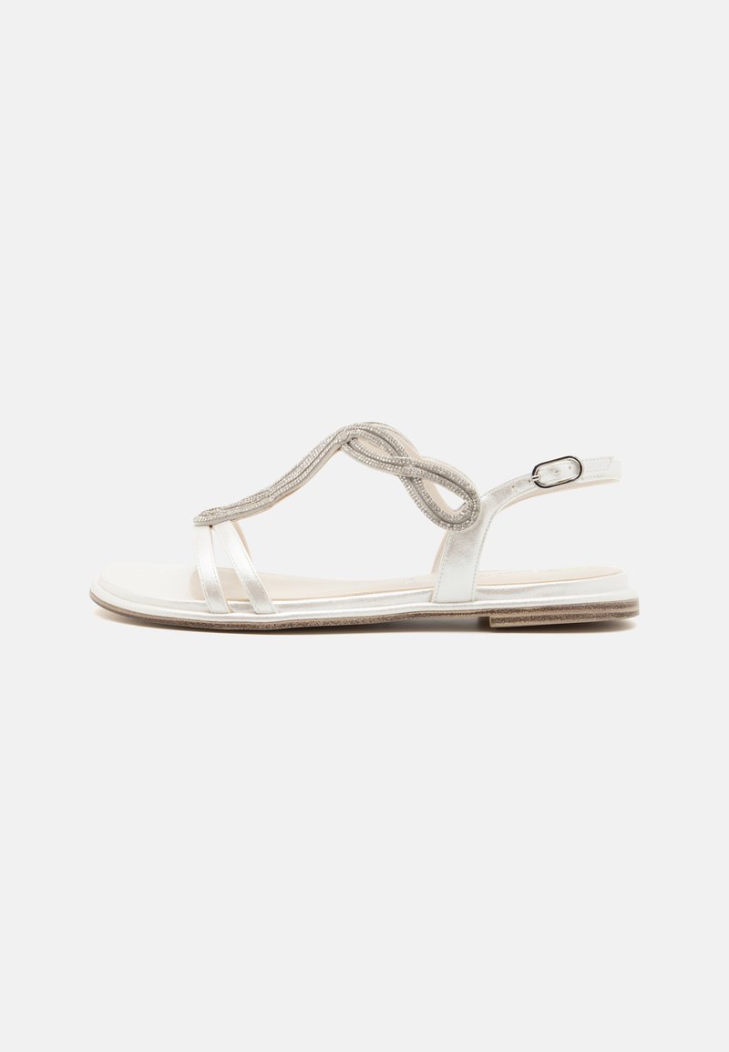 White flat sandals with shiny straps, intricate loop design, and a back buckle. Smooth sole with a slight textured edge.
