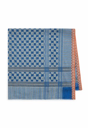 Tissu plié bleu et blanc à motifs avec des rayures et des formes en losange, avec un bord couleur rouille à motif zigzag.