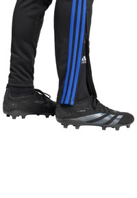 Schwarze Fußballschuhe mit silbernen Akzenten und strukturiertem Design, mit abrundeter Zehenpartie und mehreren Stollen für Traktion. Getragen mit schwarzen Sporthosen.