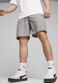Pantalones cortos grises con una textura suave, que cuentan con bolsillos laterales y un logo sutil. Combinados con zapatillas blancas y calcetines blancos acanalados.