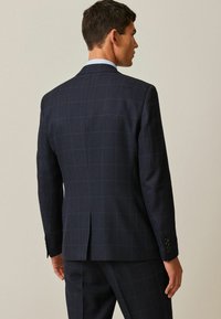 Veste de costume à carreaux marine avec un tissu texturé, deux fentes arrière et des manches à boutons. Présente une doublure de col bleu clair.