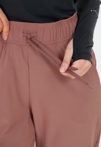 Leichte, mauve Damenhose mit elastischem Bund und Kordelzug. Glatte Stofftextur, maßgeschneidert für Komfort.