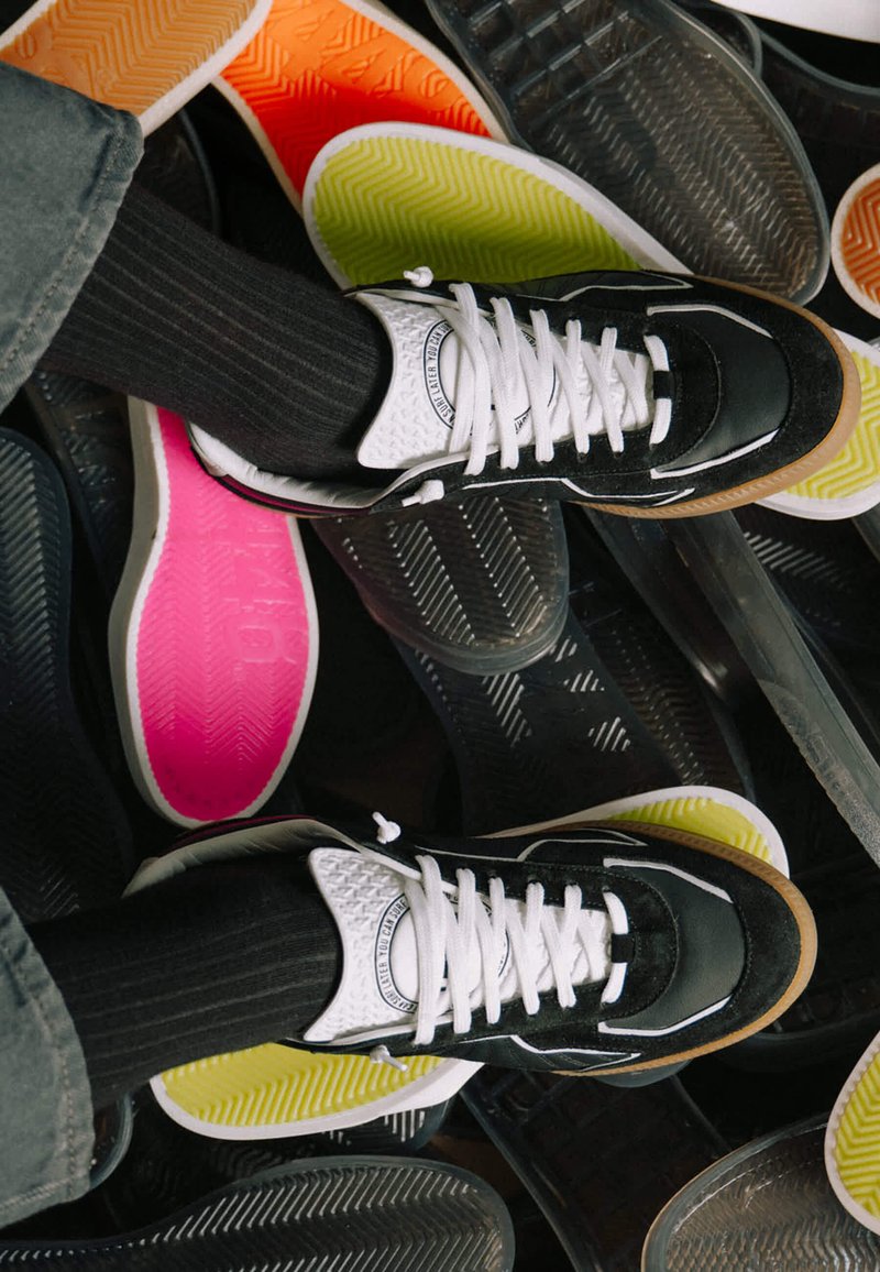 Pieds chaussés de baskets noires et blanches avec des chaussettes noires reposant sur des semelles intérieures colorées dispersées sur le sol.