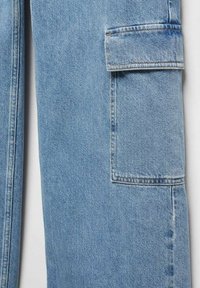 Jambe de pantalon en denim bleu clair avec une poche latérale rectangulaire munie d'un rabat sur un fond uni.