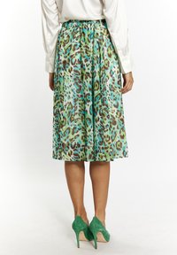 Una gonna al ginocchio con stampa leopardata verde e marrone, realizzata in un materiale leggero e setoso, abbinata a tacchi alti in suede verde.
