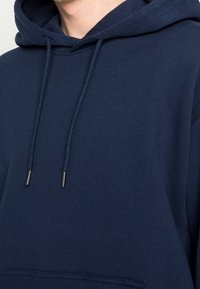 Marinblå huvtröja i mjukt tyg, med en framficka, justerbara snören med metallspetsar och ribbade muddar.