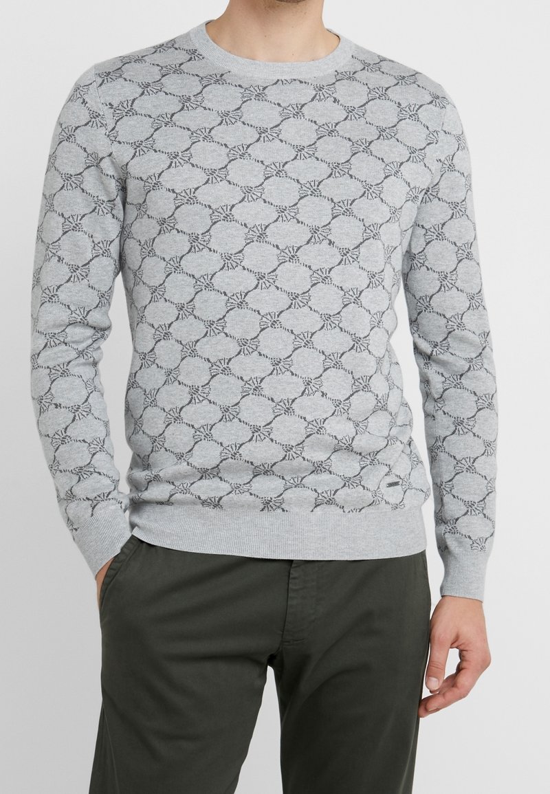 Maglione grigio chiaro con un motivo testurizzato di cerchi e linee nere, scollo rotondo, maniche lunghe e polsini e orlo a coste.