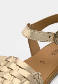Χρυσό υφαντό δερμάτινο σανδάλι με λεπτό λουράκι στον αστράγαλο και στρογγυλό μεταλλικό πόμολο, με λεία εσωτερική σόλα και επίπεδο τακούνι.