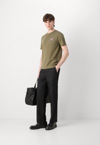 Camiseta de algodón verde olivo con acentos gráficos, combinada con pantalones cargo negros con bolsillos laterales y zapatos negros de cordones.