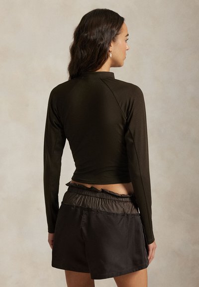 Σκούρο καφέ μπλούζα με μακριά μανίκια και ψηλό λαιμό, συνδυασμένη με μαύρο σορτς με ελαστική μέση και υφή.