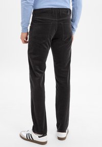 Black corduroy pants with a slim fit, featuring back pockets and a straight leg design, paired with white sneakers.