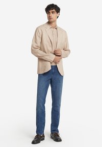 Beige linneblazer med en enkel knäppning, matchad med en krämfärgad polo, blå denimjeans och svarta snörskor.