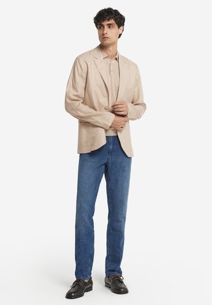 Beige linneblazer med en enkel knäppning, matchad med en krämfärgad polo, blå denimjeans och svarta snörskor.
