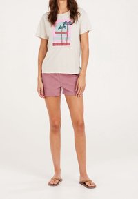 Jasnobeżowy bawełniany t-shirt z kolorowym nadrukiem palmy; zestawiony z różowymi krótkimi spodniami i brązowymi klapkami. Prosty fason i swobodny krój.