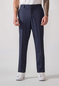 Pantalons habillés à carreaux navy avec une coupe ajustée, dotés de deux poches avant, d'un pli sur le devant et associés à des baskets blanches.