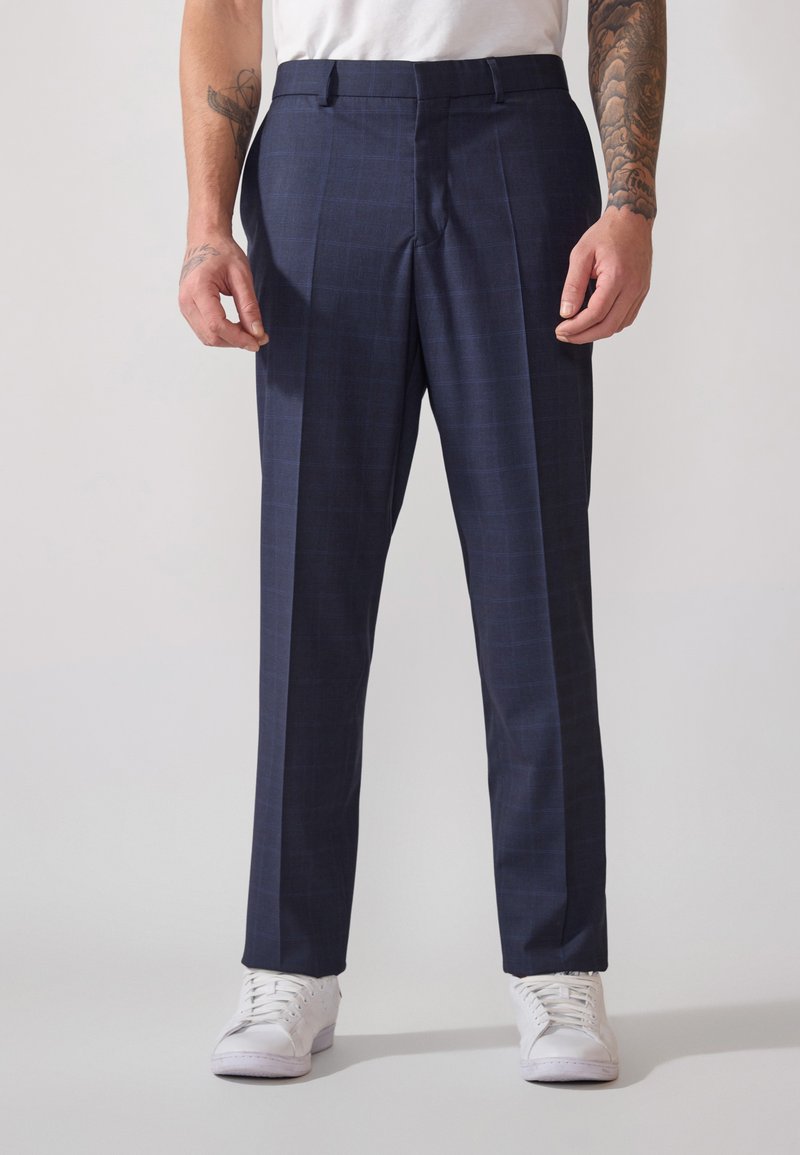 Pantalons habillés à carreaux navy avec une coupe ajustée, dotés de deux poches avant, d'un pli sur le devant et associés à des baskets blanches.
