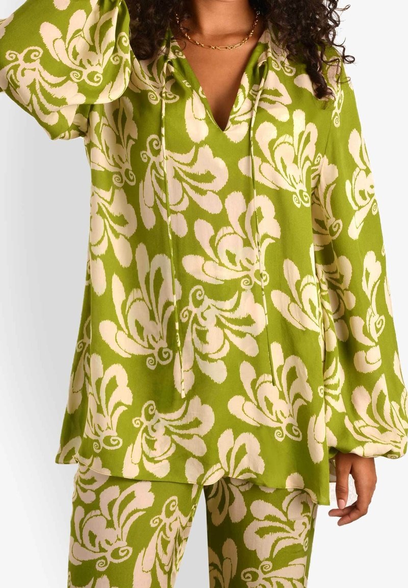Top verde a fantasia floreale con maniche a campana e scollatura a V. Il materiale appare leggero con una texture morbida. Sono visibili pantaloni floreali coordinati.