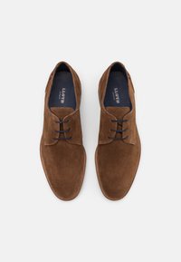 Chaussures habillées en cuir suédé marron avec une texture lisse, dotées d'un design classique à lacets et d'une couture contrastante le long de la semelle.