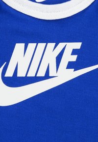 Kék szövet póló fehér körkivágással, kiemelkedő fehér "NIKE" logóval és alatta egy swoosh mintával.