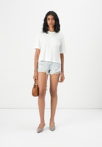 T-shirt blanc à manches courtes avec broderie florale, shorts en denim léger, ballerines beiges à bout pointu, et un petit sac à main marron. Style minimaliste.