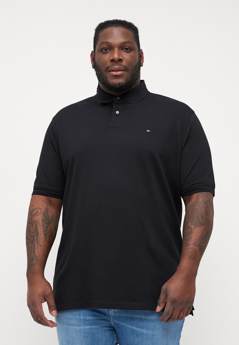 Sort polo-shirt med en to-knaps placket, korte ærmer, blødt stof og lille logo på brystet. Bæres med lyseblå jeans.