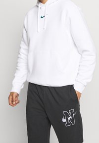 Vit hoodie med känguruficka och teal Nike-logga; matchas med mörkgrå sweatpants med vit "N"-logga och accent.