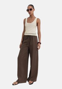 Top de punto crema con un corte holgado, combinado con pantalones de pierna ancha marrones. Los accesorios incluyen gafas de sol grandes y una pulsera marrón.
